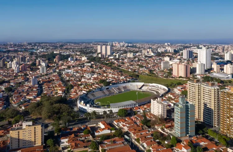 Imagem da cidade de Campinas com o Estádio Moisés Lucarelli, como ponto central. Ao redor do estádio, há uma paisagem com prédios e algumas áreas verdes visíveis.